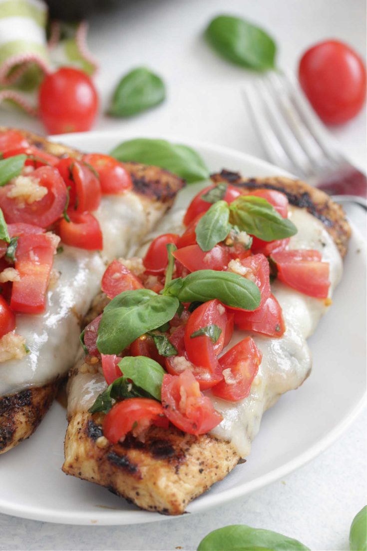 Bruschetta Chicken on a white plate with tomatoes and basil on top