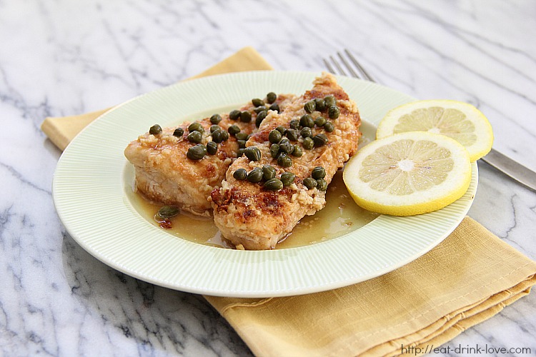 Chicken Piccata on a green plate with lemon slices and capers on top