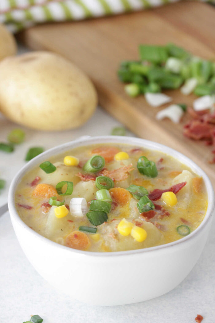 Low Fat Corn and Potato Chowder in a bowl with potatoes and sliced green onions in the background