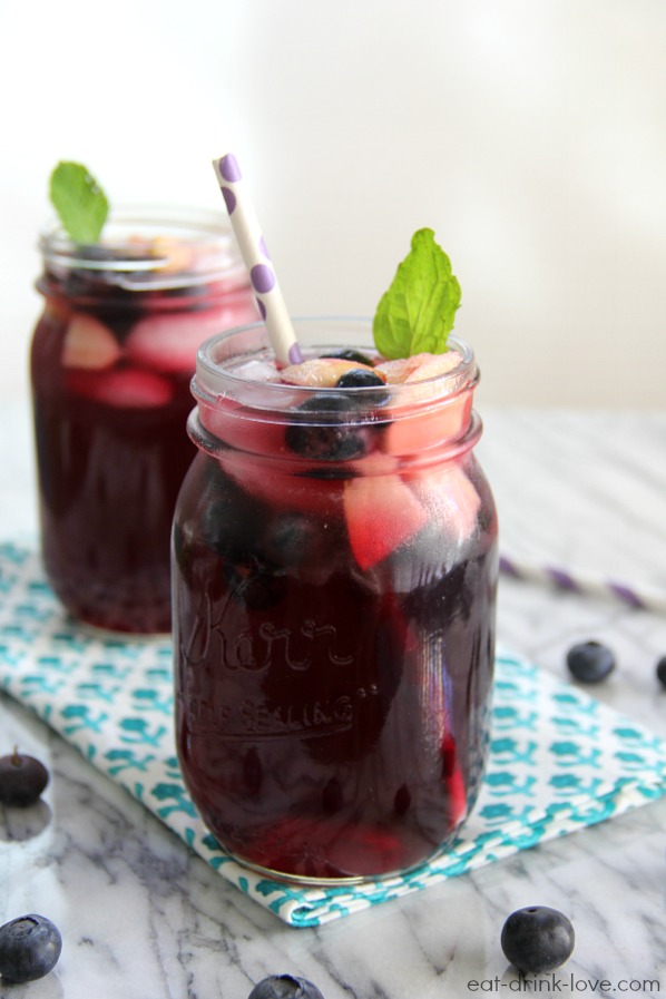 Blueberry Pomegranate Sangria in jar with a straw, fruit, mint leaves