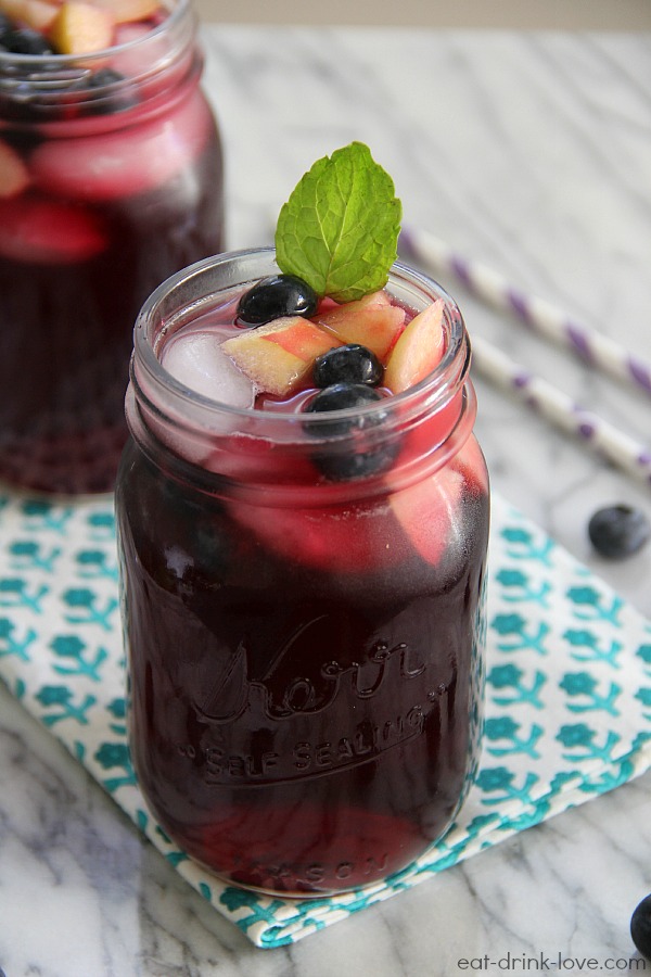 Blueberry Pomegranate Sangria in jar with a straw, fruit, mint leaves