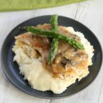 Chicken Madeira on a blue plate with mashed potatoes and asparagus on top