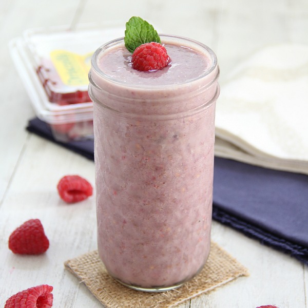 Raspberry Almond Smoothie in a glass jar with fresh raspberries on a white board