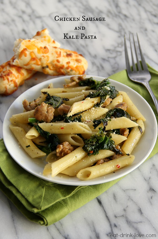Chicken Sausage and Kale Pasta on a white plate with a bread stick