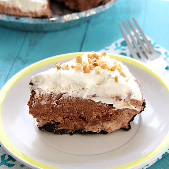 No-Bake Chocolate Peanut Butter Pie sliced on a white plate topped with whipped cream and chopped peanuts