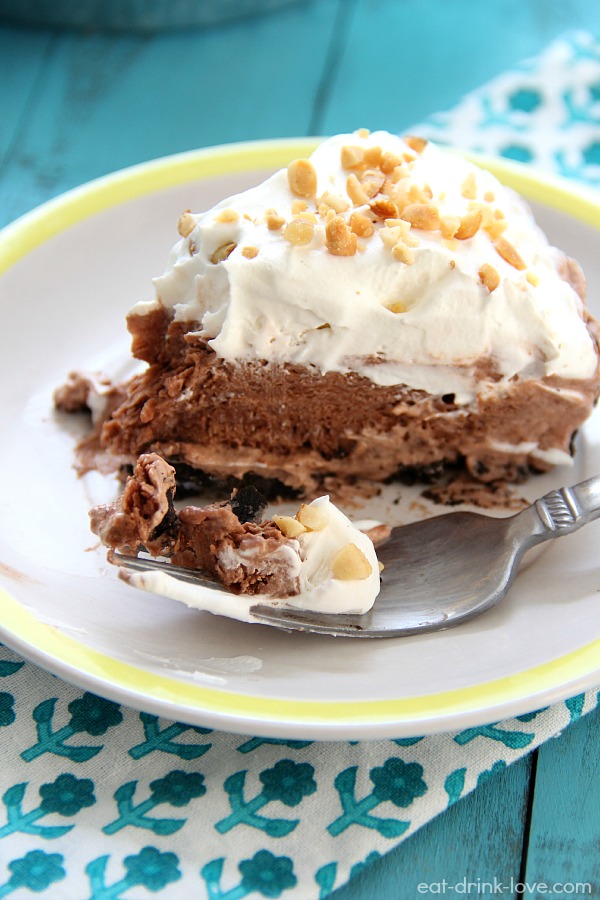 No-Bake Chocolate Peanut Butter Pie sliced on a white plate topped with whipped cream and chopped peanuts and a fork