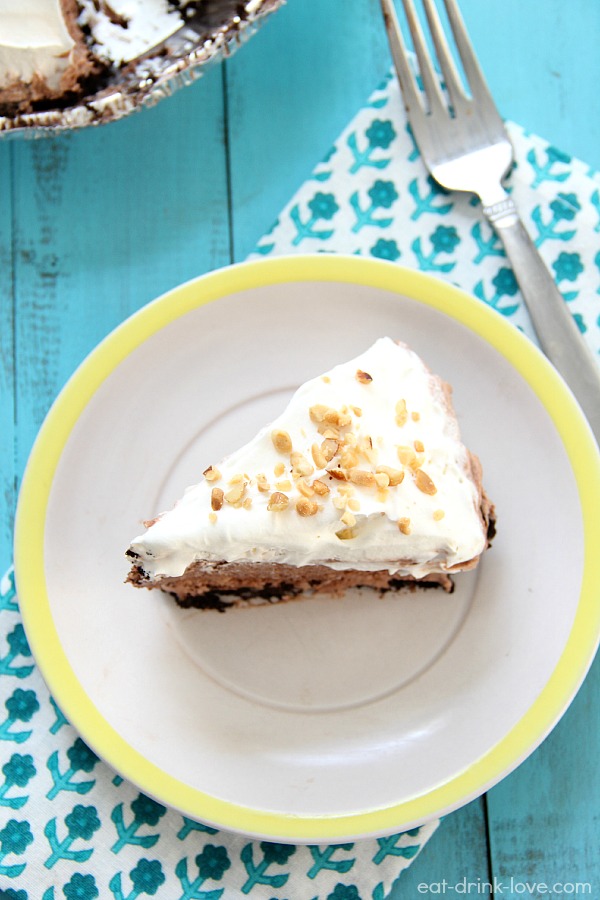 No-Bake Chocolate Peanut Butter Pie sliced on a white plate topped with whipped cream and chopped peanuts on a turquiose board