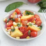 Peach and Tomato Salad on a white plate with basil and peaches