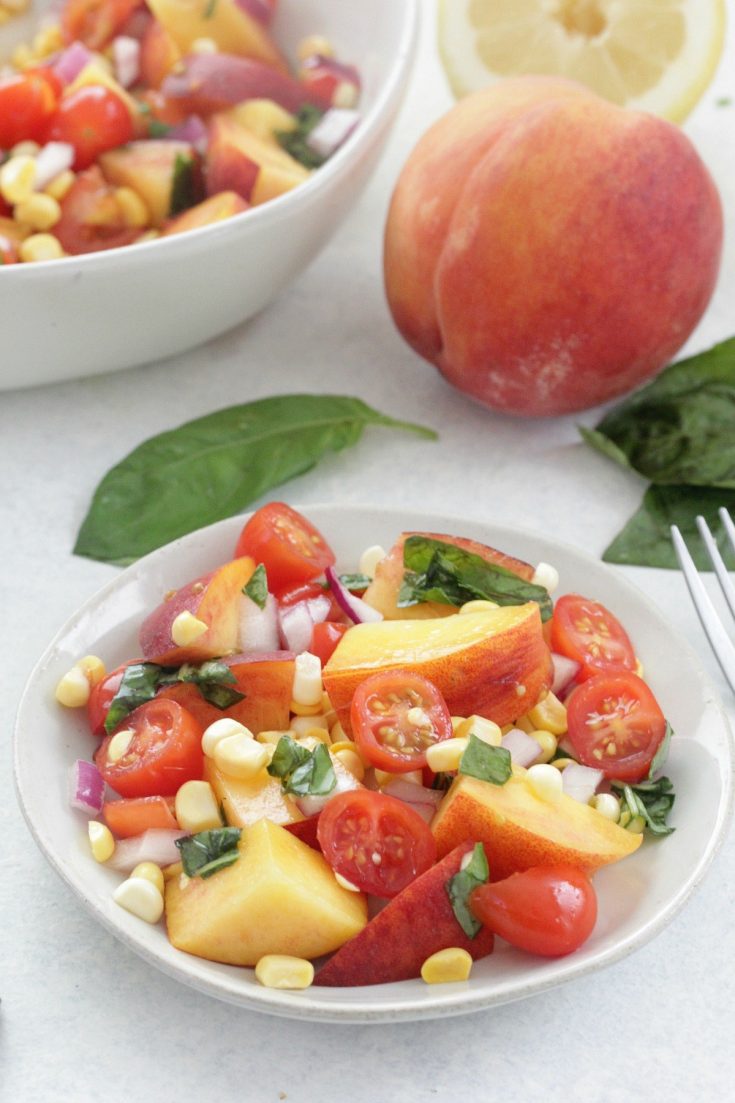 Peach and Tomato Salad on a white plate with fresh basil leaves and a peach