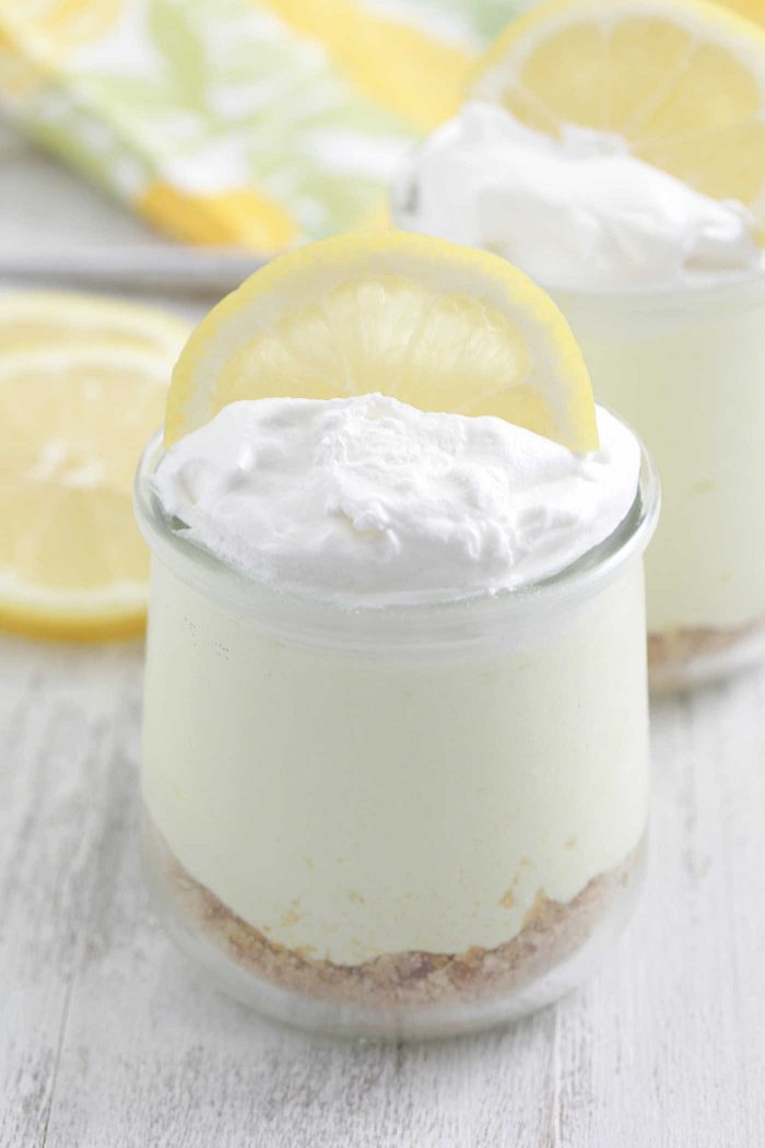 No-Bake Lemon Cheesecakes in glas jars with whipped cream and lemon slices