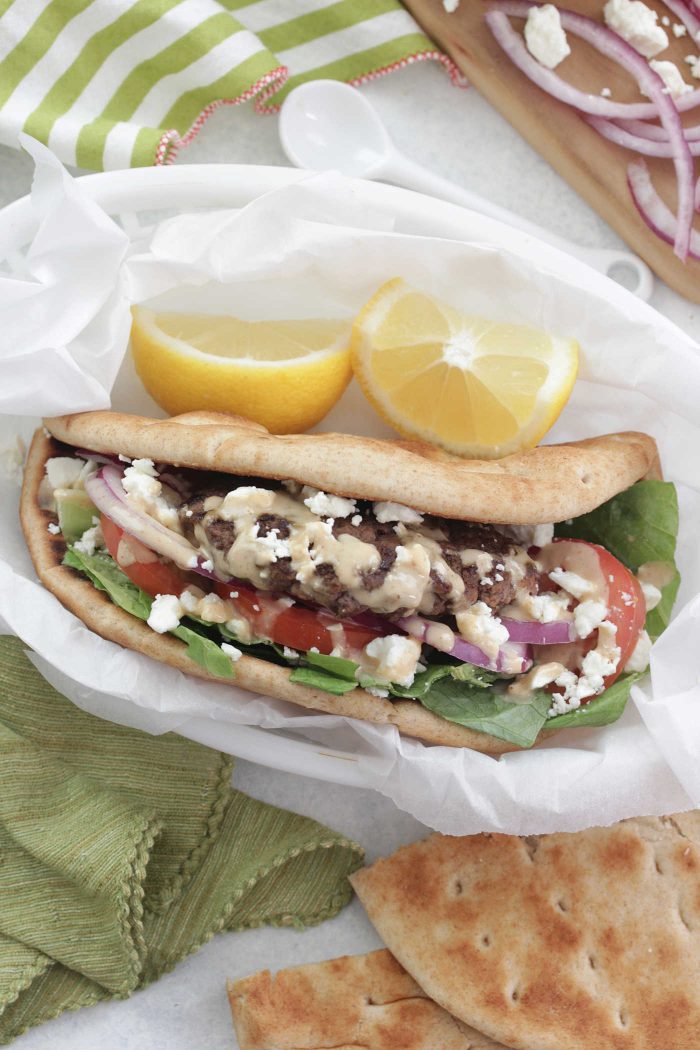 Overhead shot of Greek Burgers in a pita with feta, lemon, tomato in a white basket