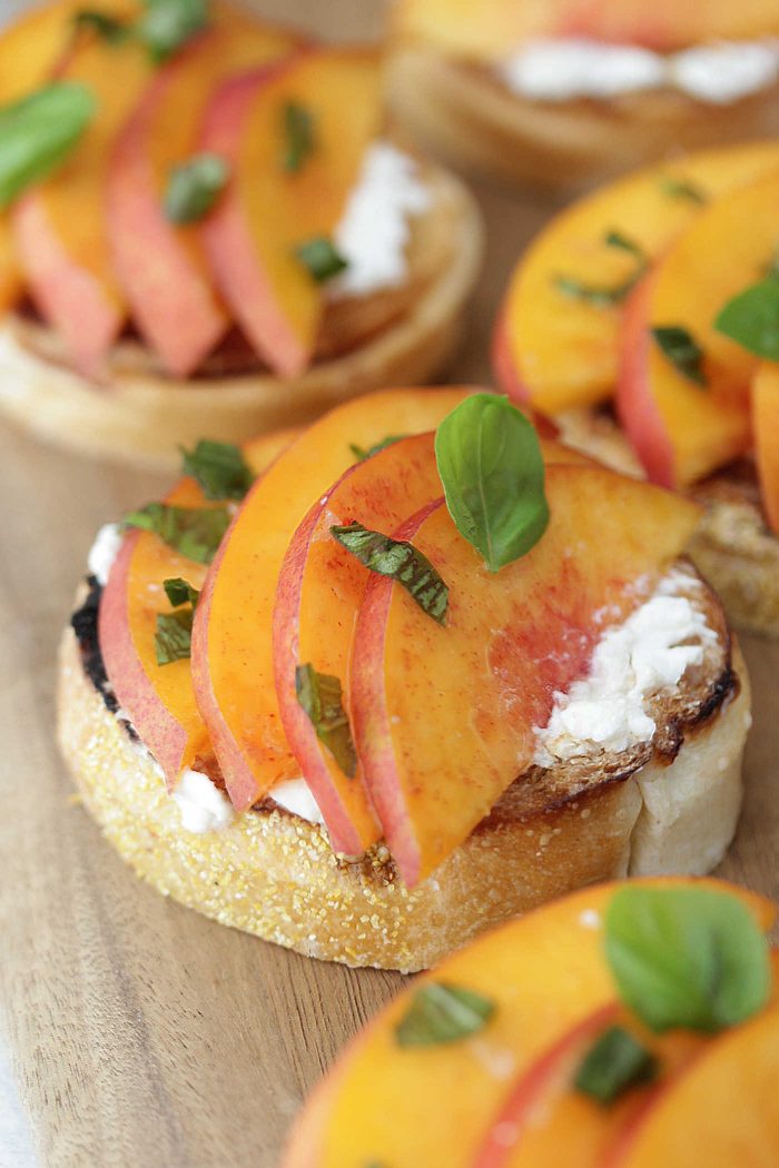 Peach Burrata Toasts on a wooden board topped with chopped basil