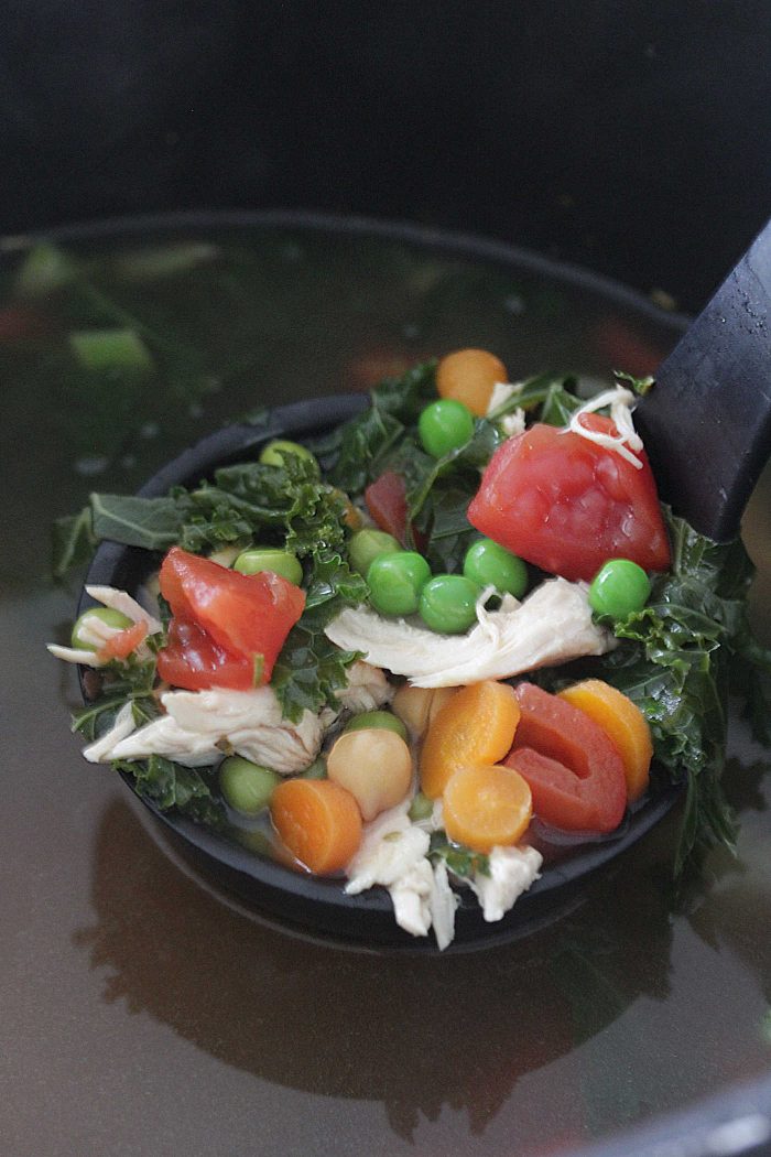 Chicken Veggie Soup in a soup spoon with chicken peas carrots tomatoes and kale
