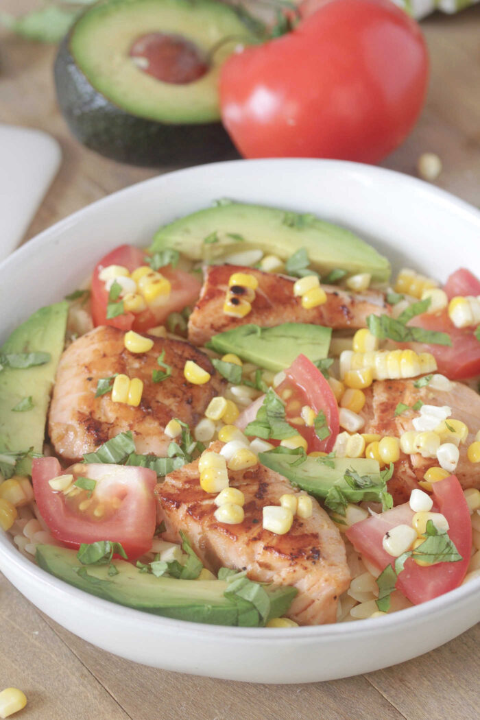 Close-up shot of grilled salmon orzo bowls with corn, tomatoes, and avocado