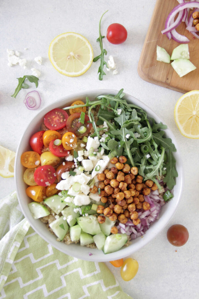overhead shot of Quinoa & Arugula Salad with Crispy Chickpeas in a white bowl with sliced lemons on the side