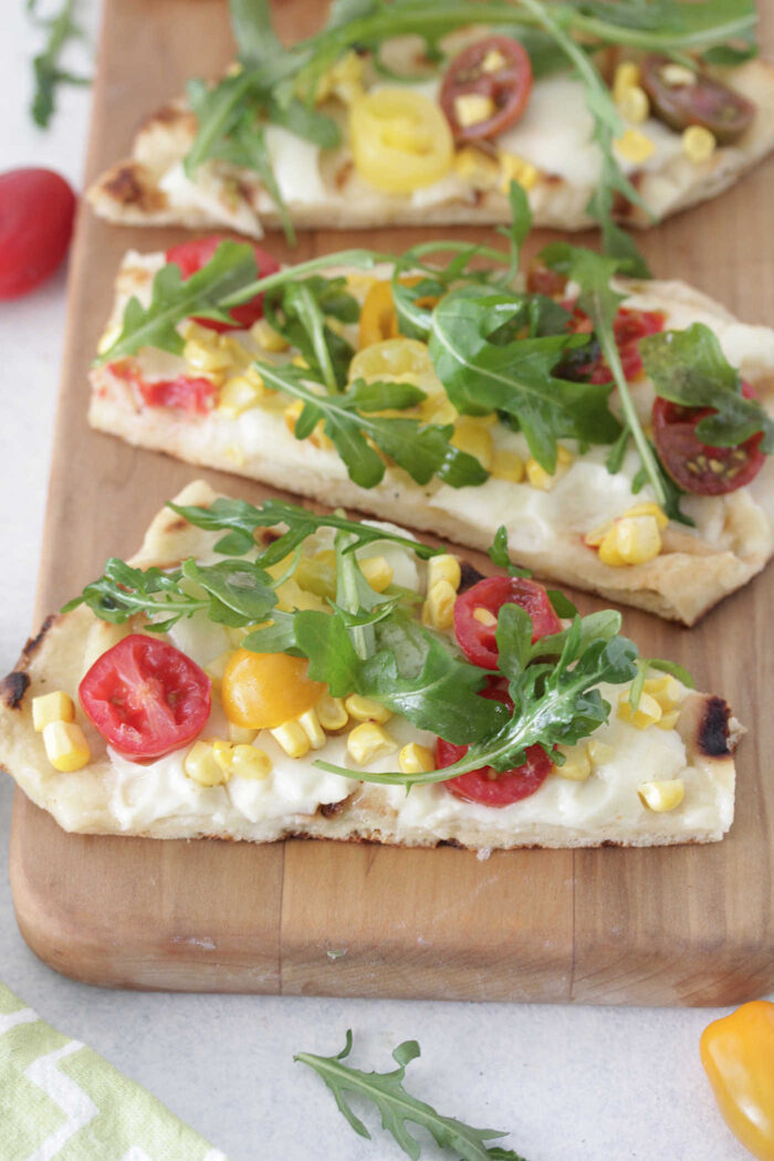 Angled photo of grilled summer flatbread pizzas topped with fresh arugula