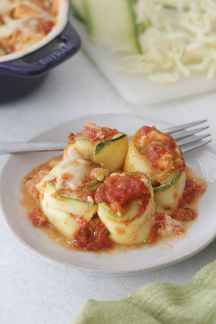 Zucchini Lasagna Roll Ups on a white place with tomato sauce on top