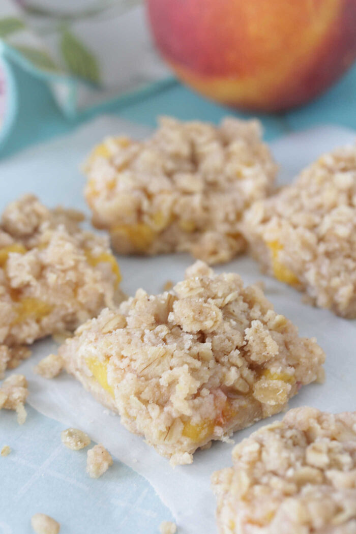 Sliced Peach Crumble Bars on parchment paper with a peach and floral napkin in the background