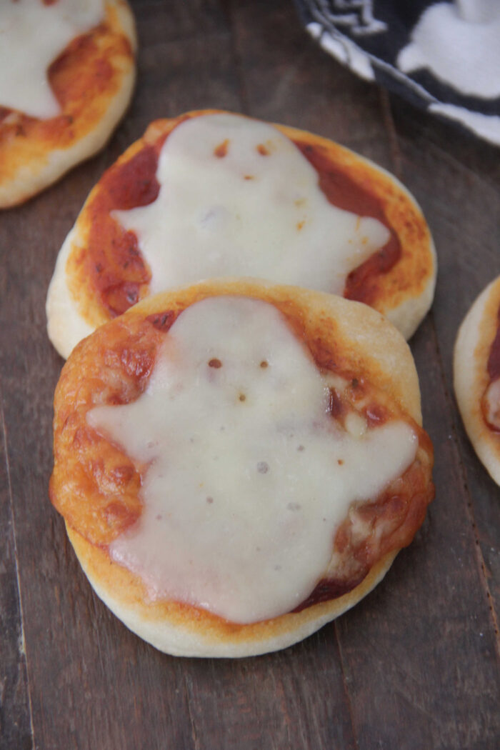 Angled photo of mini pizzas with a slice of cheese cut into the shape of a ghost