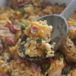 Close up shot of a wooden spoon scooping loaded chicken cauliflower casserole