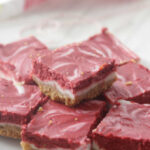 Skinny Red Velvet Cheesecake Bars arranged on a white dish with a heart napkin in the background