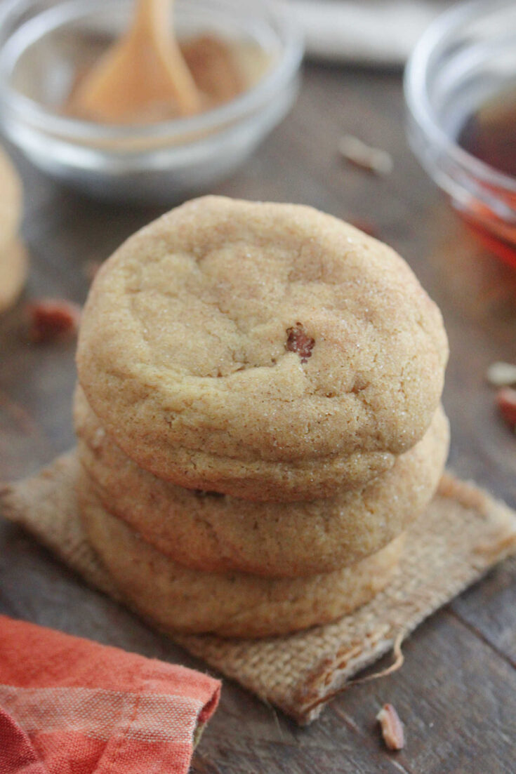 Brown Butter Maple Pecan Pumpkin Cookies stacked on a wooden table with chopped pecans scattered around