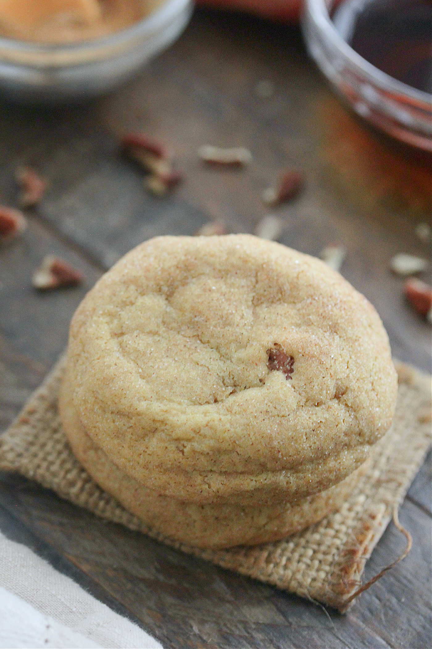Brown Butter Maple Pecan Pumpkin Cookies stacked on a wooden board with maple syrup and cinnamon sugar