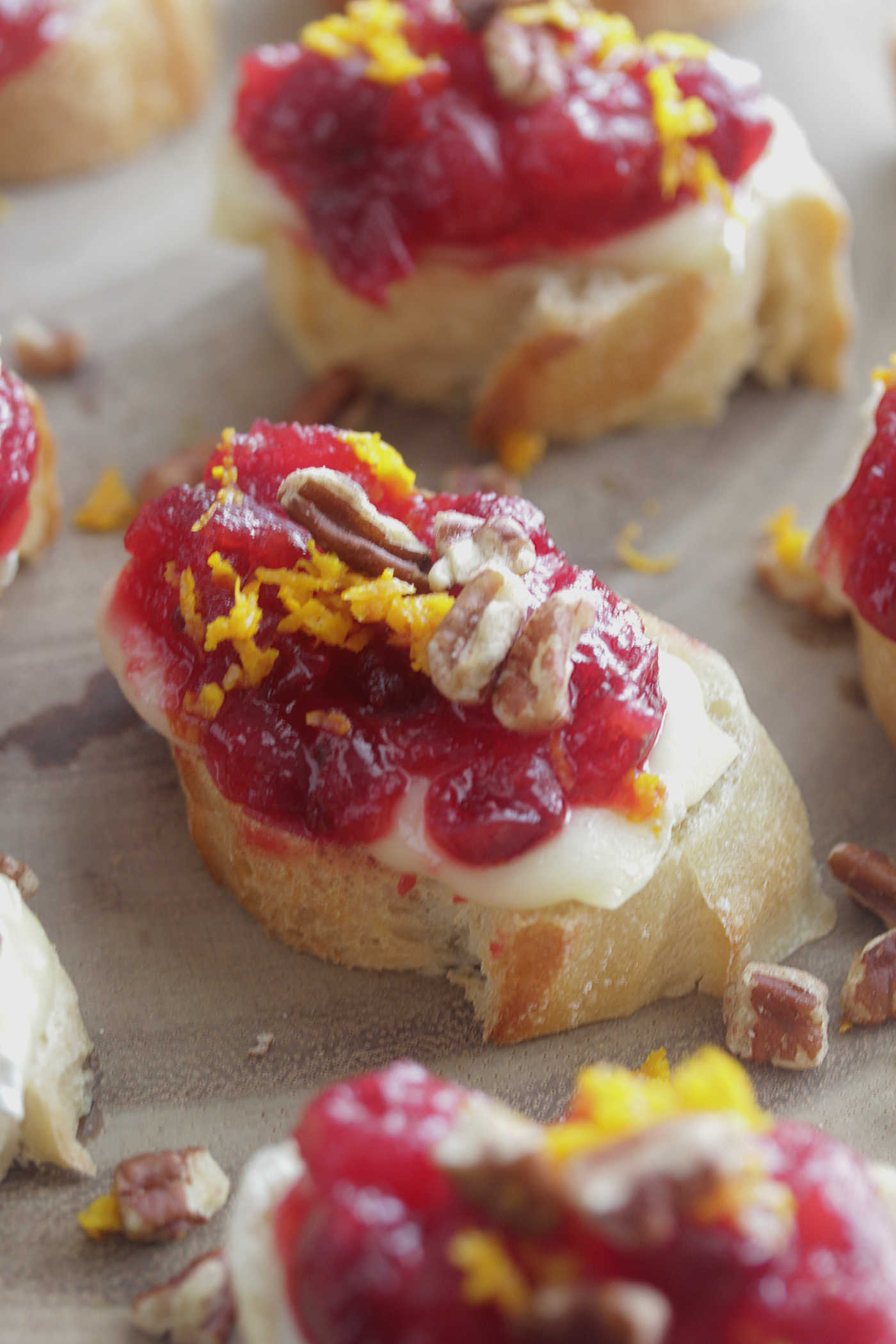 Cranberry Orange Brie Crostini on a wooden board with orange zest and pecans