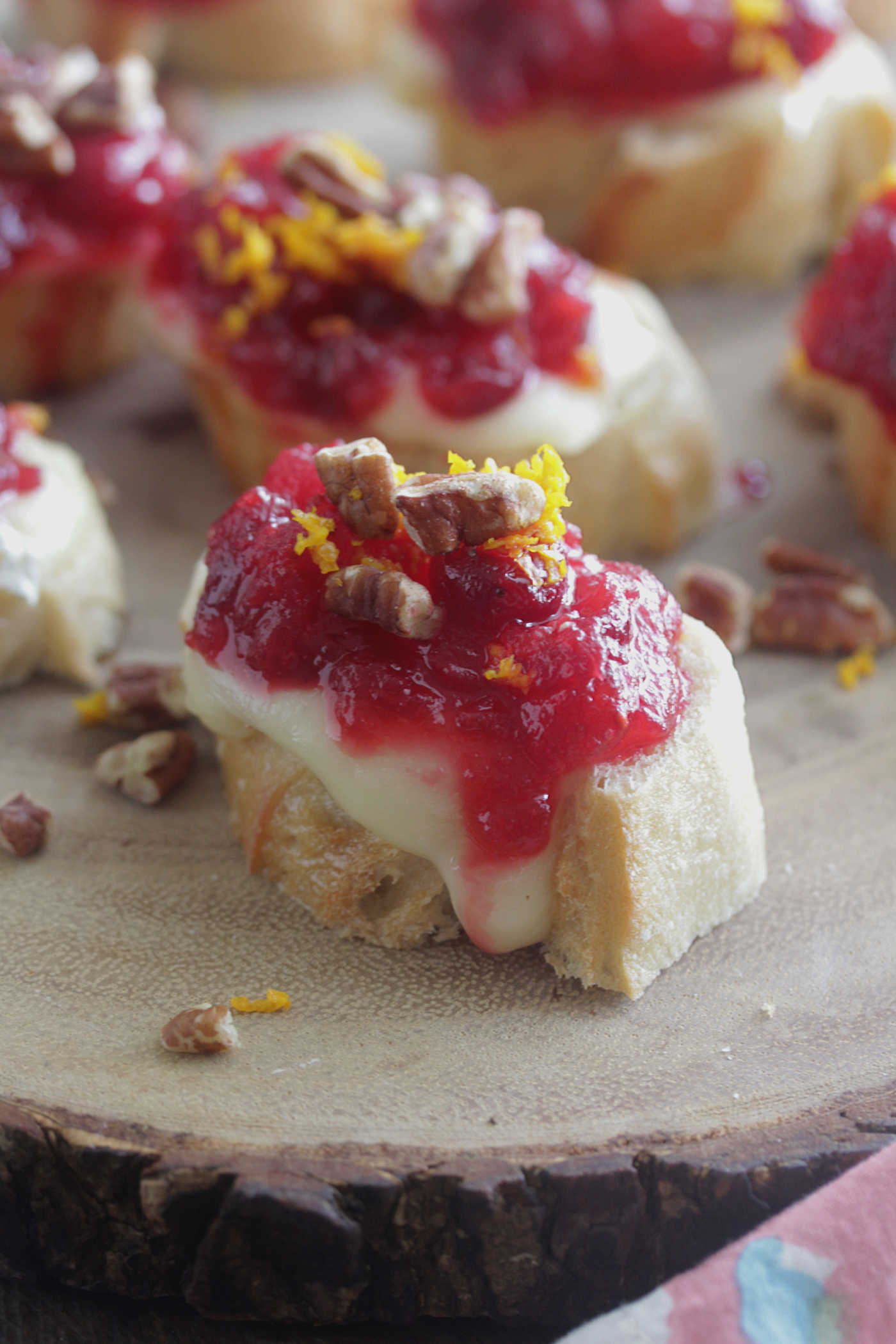 Close up Cranberry Orange Brie Crostini on a wooden board with orange zest and pecans