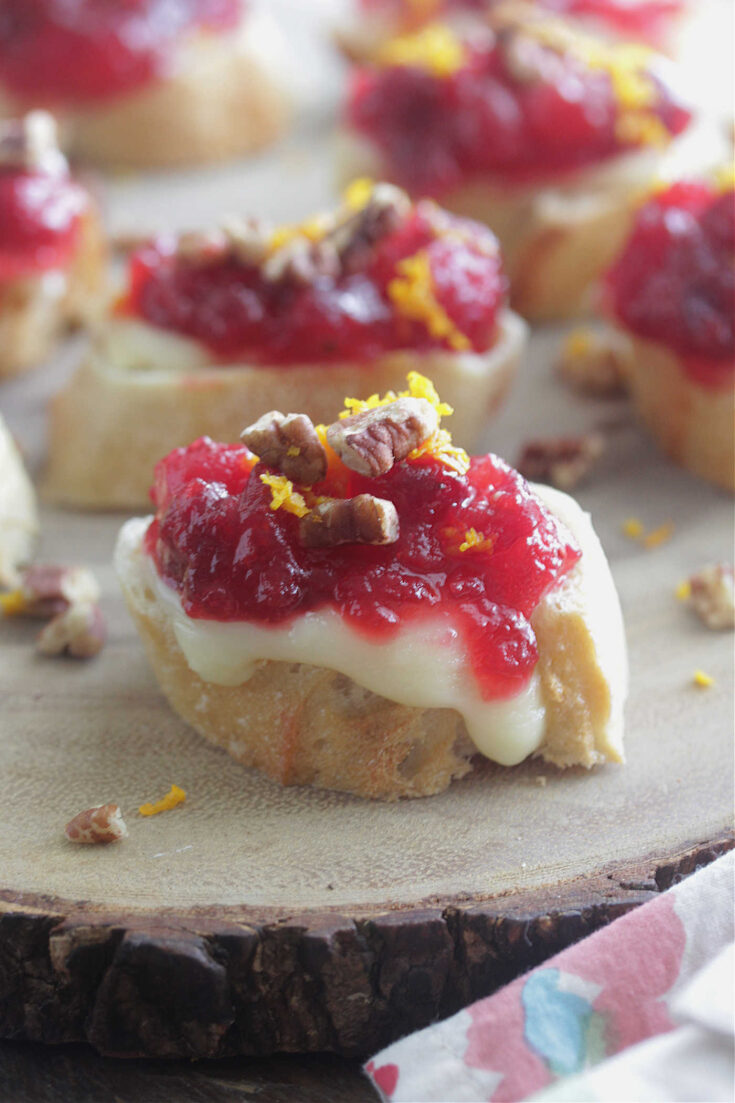 Cranberry Orange Brie Crostini on a wooden board with orange zest and pecans