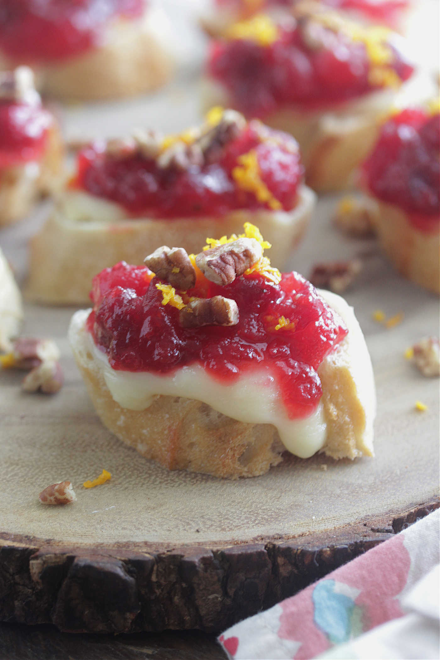 Cranberry Orange Brie Crostini on a wooden board with orange zest and pecans