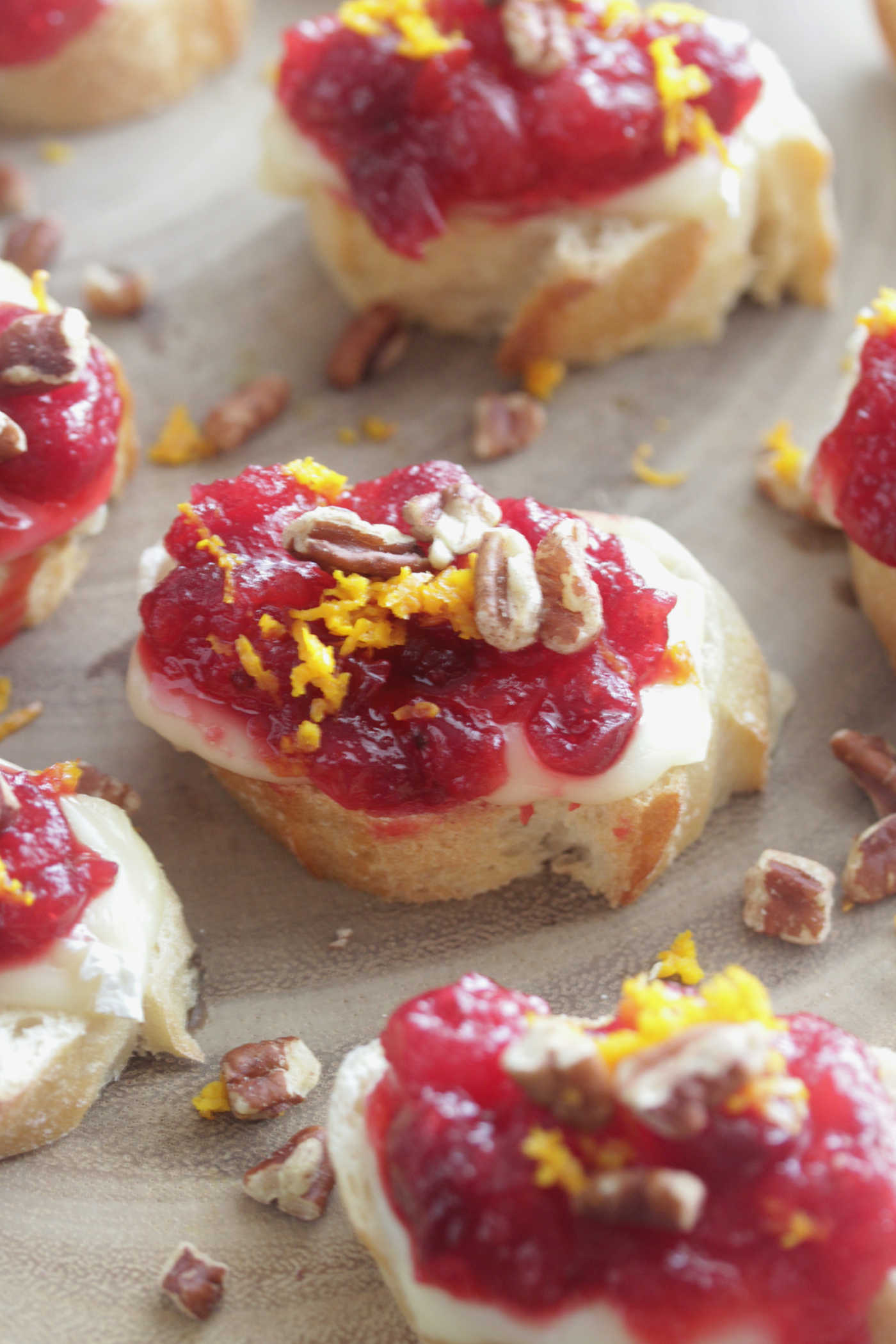 Cranberry Orange Brie Crostini on a wooden board with orange zest and pecans