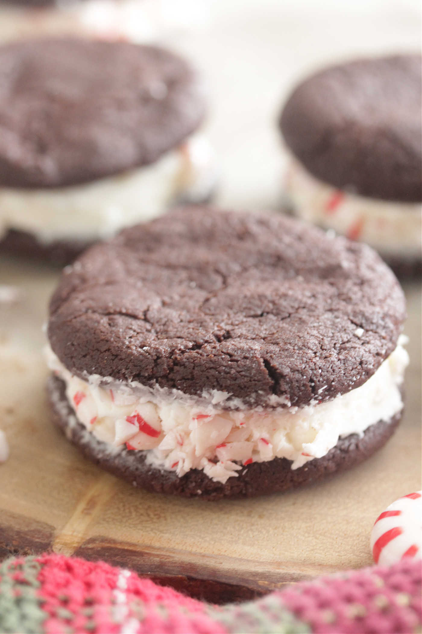 Chocolate Peppermint Sandwich Cookies arranged on a wooden board with crushed peppermint candies and a festive napkin