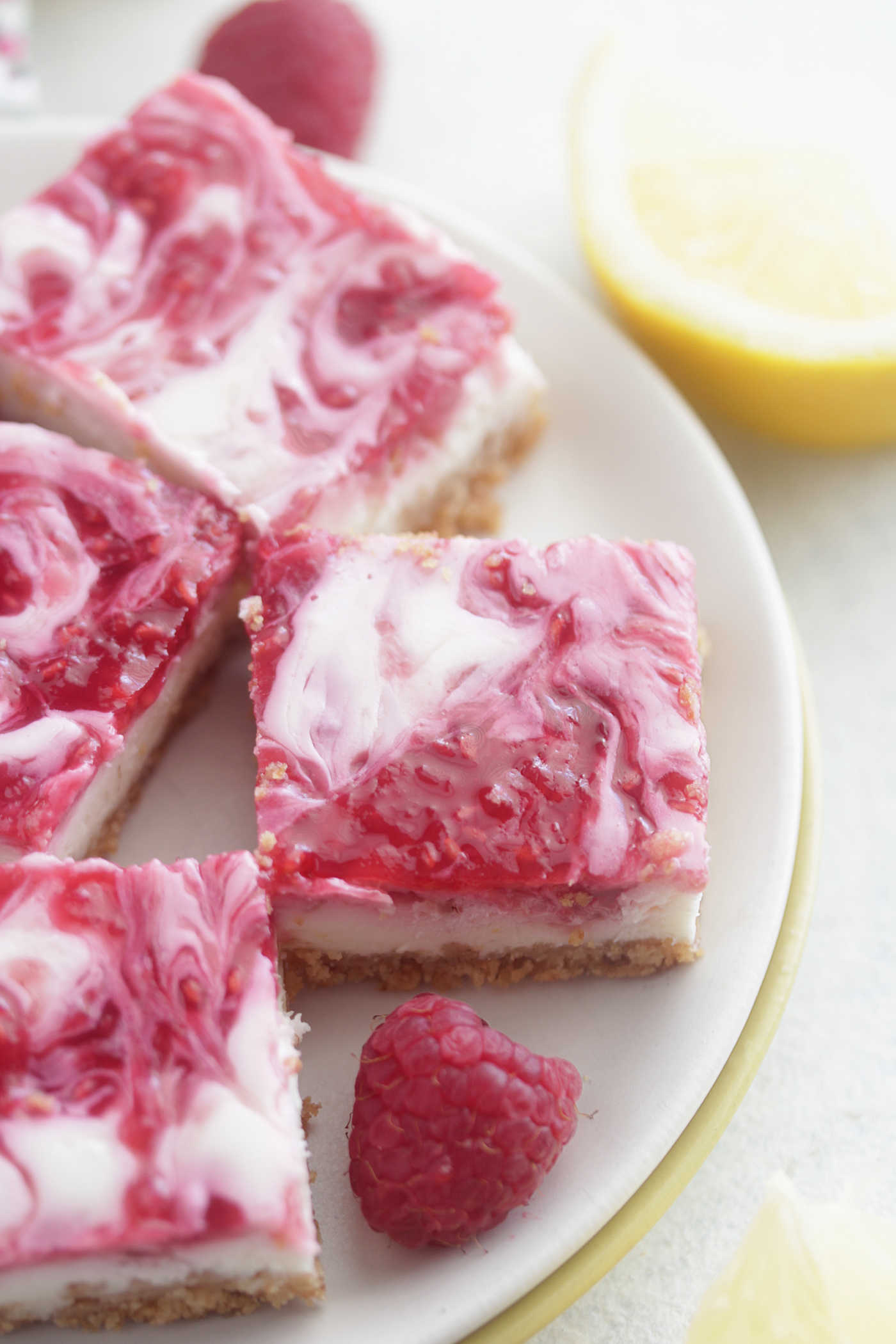 Close-up photo of lower fat lemon raspberry cheesecake bars on a plate with fresh raspberries and lemon slices