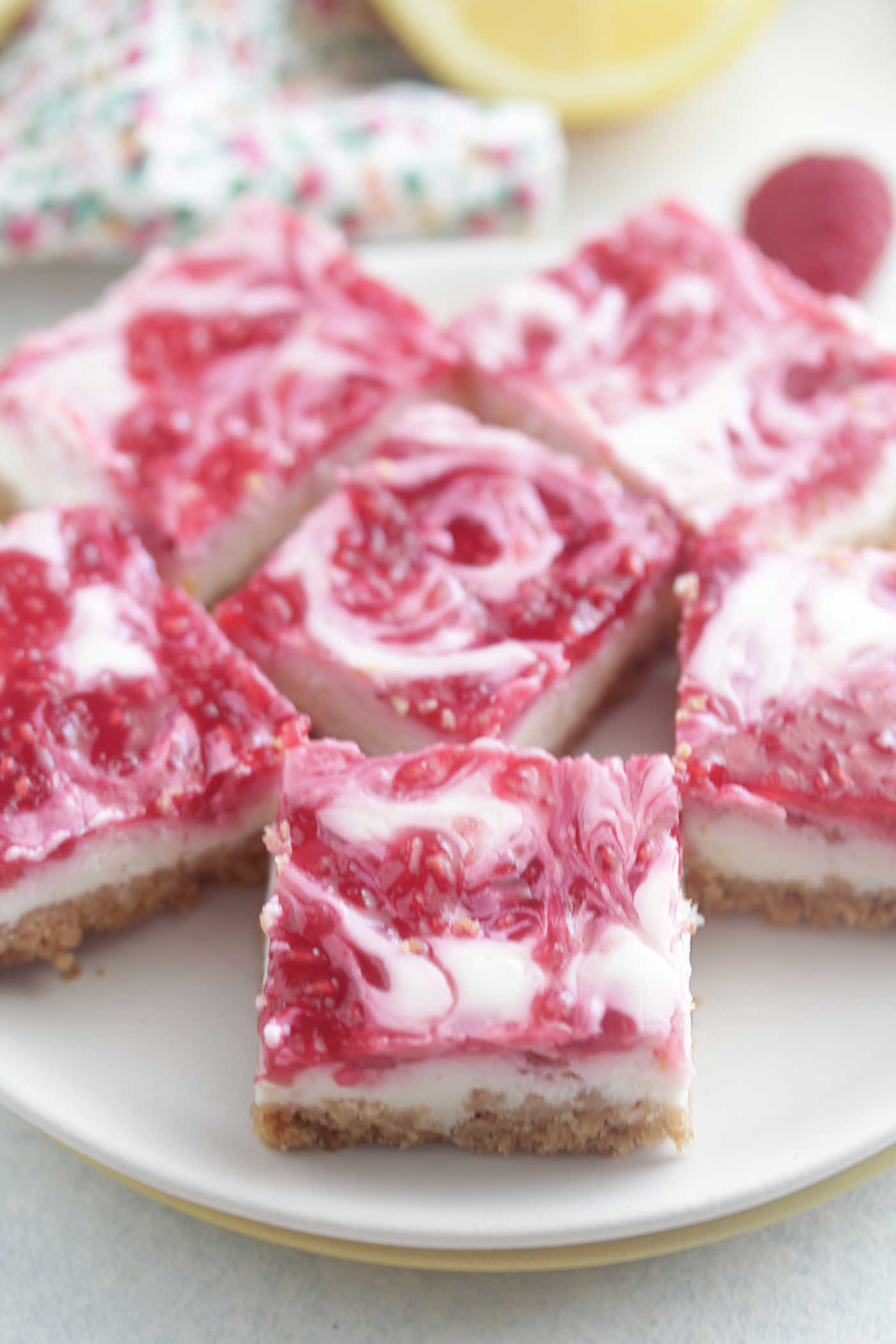 Skinny Lemon Raspberry Cheesecake Bars arranged on a white plate with lemon slices