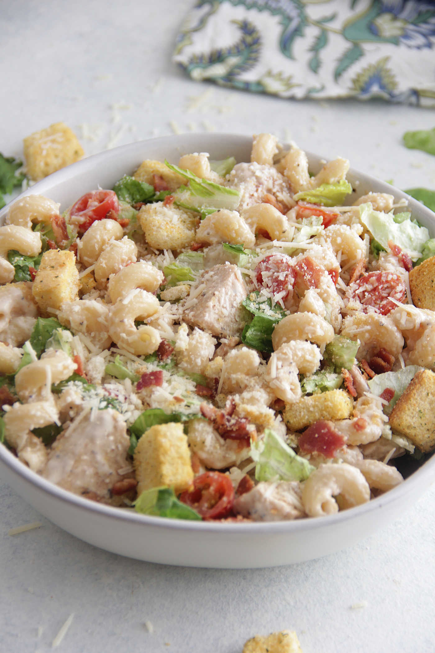 Close up photo of chicken caesar pasta salad in a large bowl with tomatoes and croutons.