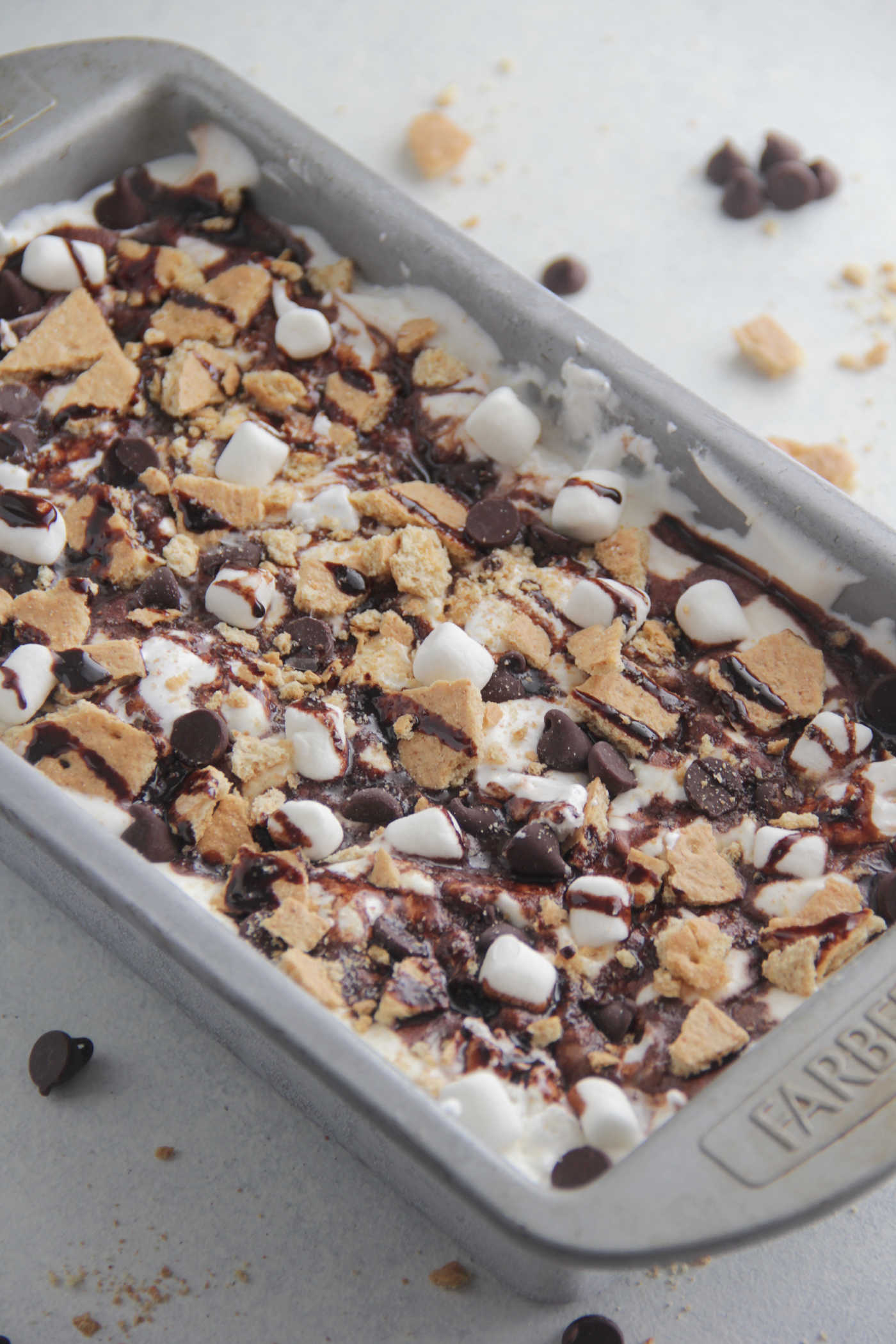 S'mores No-Churn Ice Cream in a metal tin with lots of chocolate syrup, graham cracker chunks, and chocolate chips