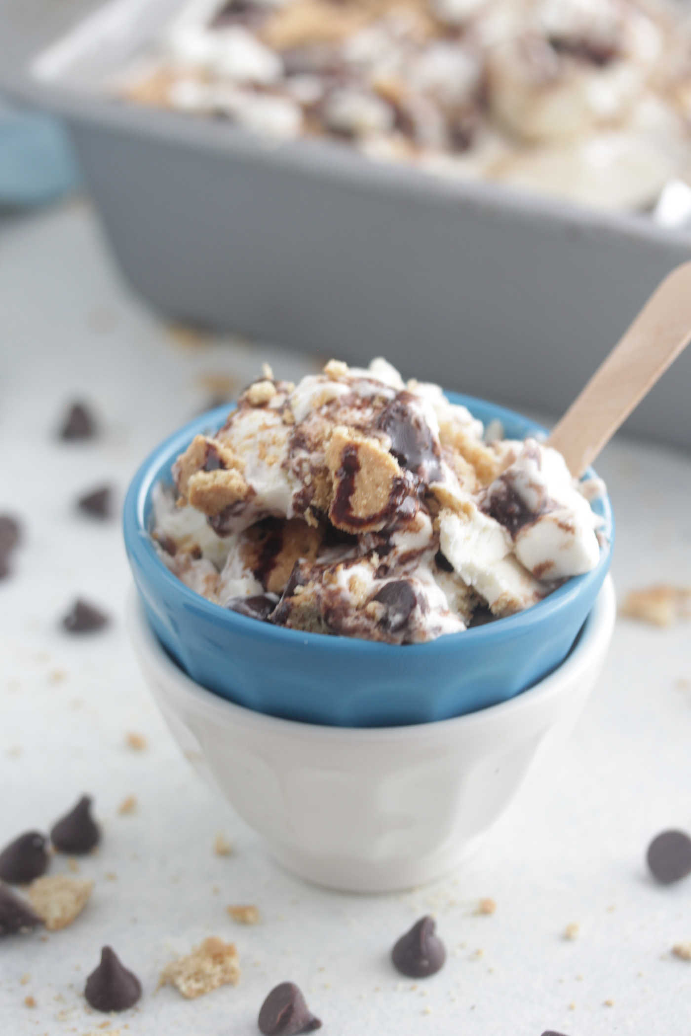 A bowl of s'mores no-churn ice cream with mini marshmallows, chocolate chips and syrup, and a wooden spoon