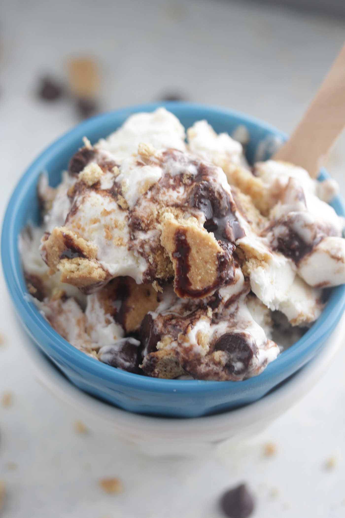 A close-up photo of s'mores ice cream in a bright blue bowl with a wooden spoon