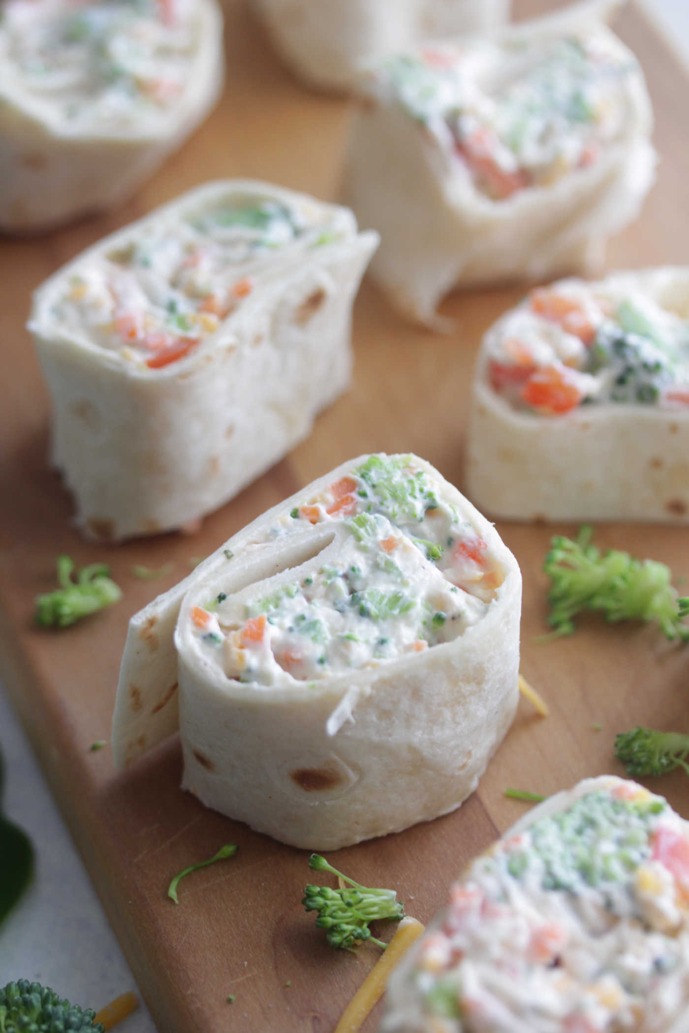 Angled shot of veggie roll ups on a wooden board with shredded broccoli arranged around the side