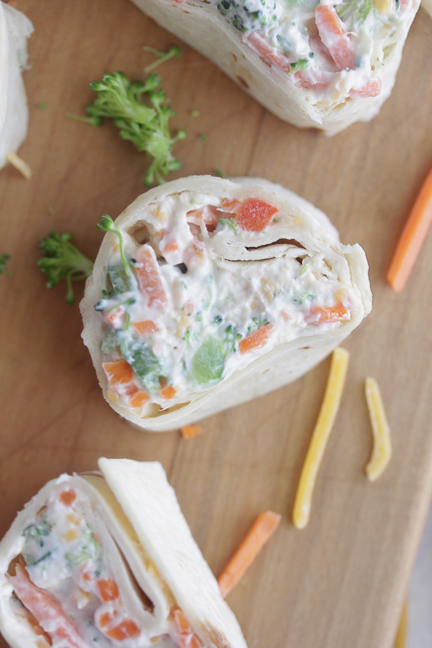 Overhead photo of veggie roll ups on a wooden board with shredded carrots and cheese around it