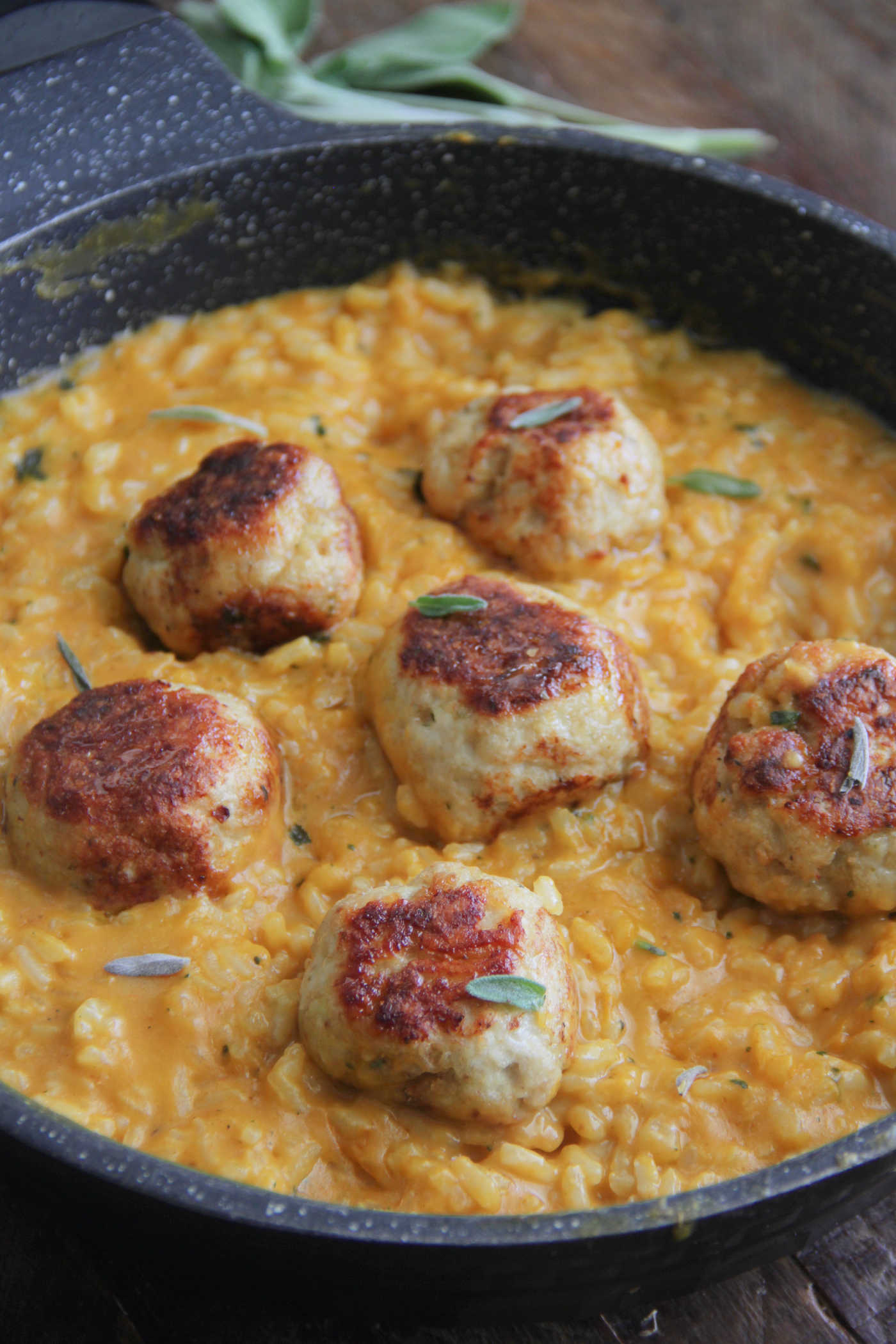 Close up shot of chicken meatballs in a pan with creamy pumpkin risotto and sage on top.