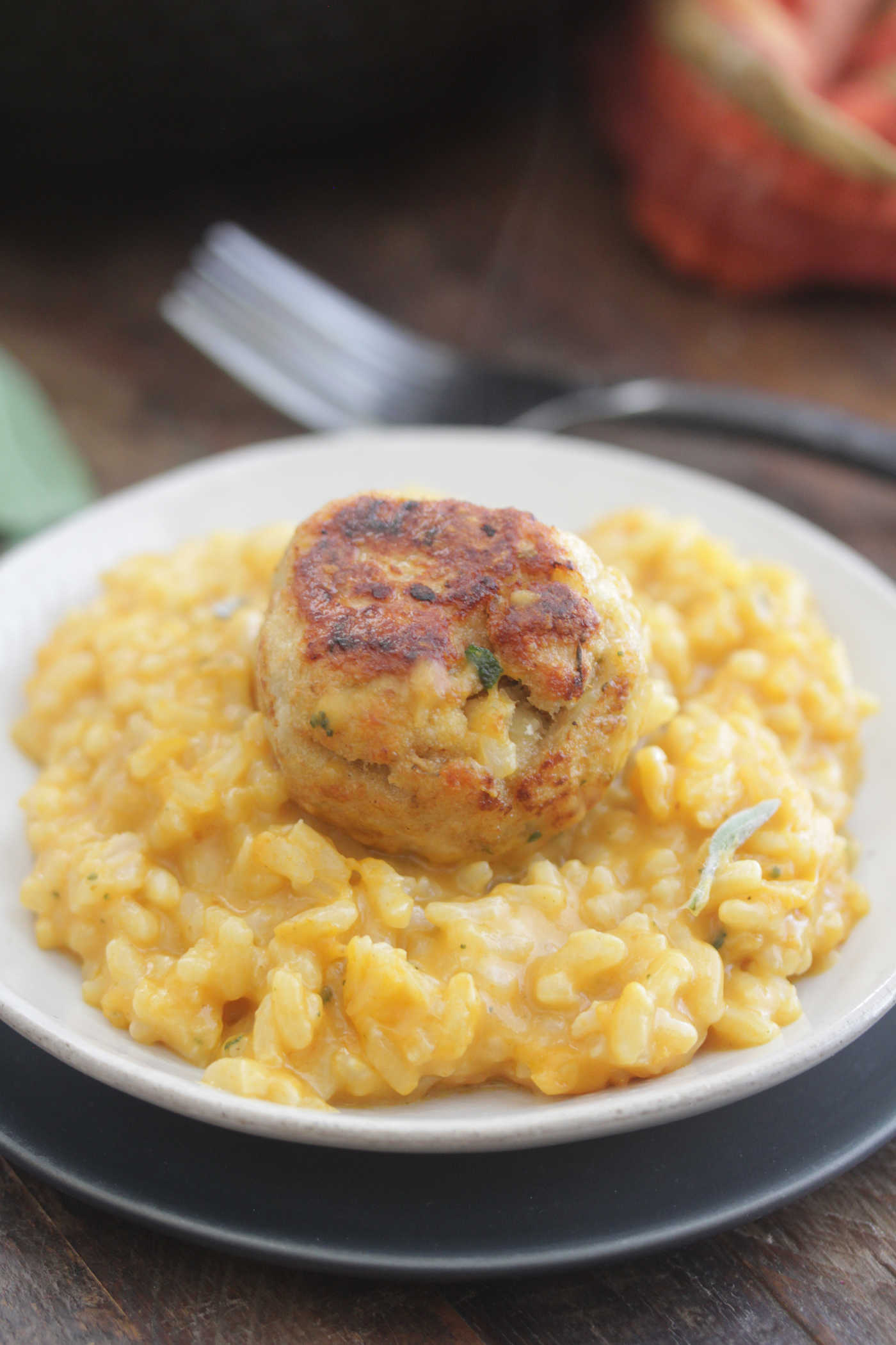 Pumpkin risotto on a white plate with a chicken meatball on top.